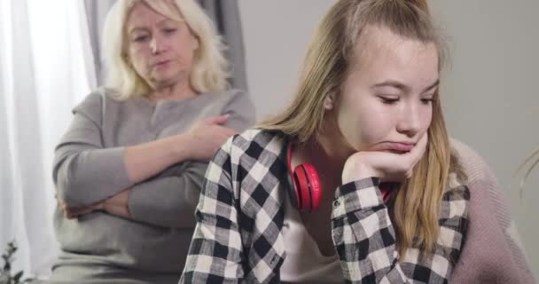 Retrato de cerca de una joven caucásica ignorando a la abuela sentada al fondo. Mujer rubia madura tocando nietas hombro y dando la espalda. Generaciones. Sede del cine 4k ProRes . — Vídeos de Stock