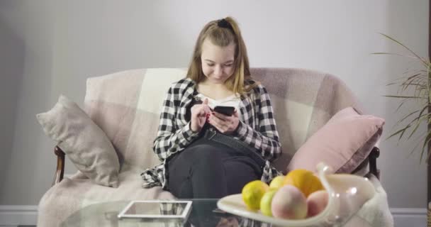 Portrait of cute Caucasian girl sitting on sofa and using smartphone as unrecognizable mature woman coming up. Grandmother asking granddaughter to stop using social media. Cinema 4k ProRes HQ. — 비디오