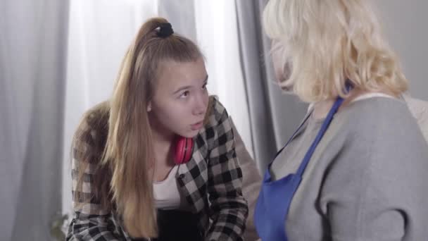Närbild av söt vit tjej som pratar med blond mogen kvinna. Mormor kramar barnbarn och tittar bort. Stöd, omsorg, familjerelationer. — Stockvideo