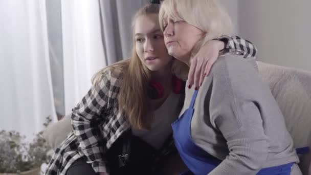 Retrato de una joven caucásica abrazando a la abuela. Nieta feliz pasar tiempo libre con la mujer rubia de alto nivel en el interior. Buena relación, generaciones, familia . — Vídeo de stock