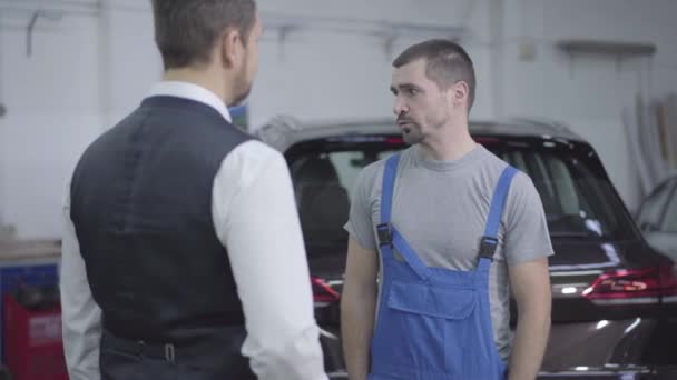 Kafkasyalı genç bir adam tamirhanede müşterilerin araba anahtarlarını alıyor ve elini sıkıyor. Tamir için araba tamircisi alıyor. Araba işi, tamir hizmetleri.. — Stok video