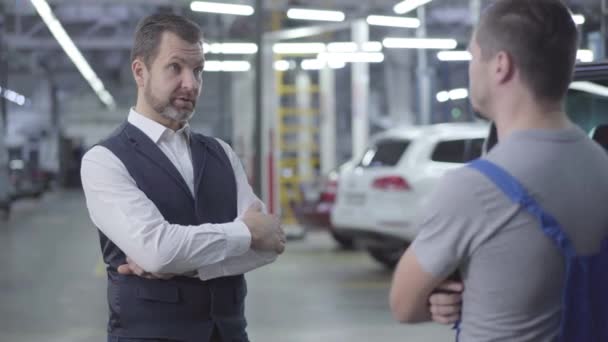 Sparando alle spalle del meccanico caucasico dando le chiavi della macchina al proprietario e stringendo la mano. Lavoratore che restituisce l'automobile dopo riparazione della garanzia. Servizio, officina . — Video Stock