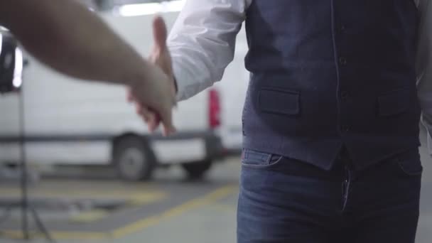 Close-up of two Caucasian men shaking hands in car repair shop. Male hands at the background of vehicles. Car business, auto showroom, repair services. — 비디오