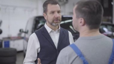 Tanımlanamayan araba tamircisiyle konuşan Kafkasyalı adamın yakın plan portresi. Yetişkin, kendine güvenen işadamı tamirhaneden memnun değil. Garanti, araba işi..