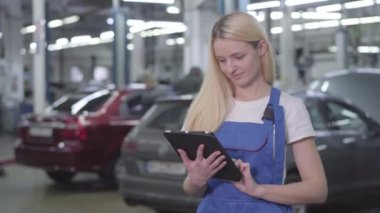 Üzerinde tablet olan beyaz elbiseli, gülümseyen genç bir kadın kameraya bakıyordu. Araba tamirhanesinde çalışan profesyonel kadın tamirci. Profesyonel, garanti hizmetleri.