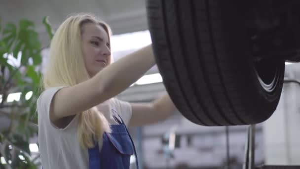 Portrait of young beautiful Caucasian woman tightening screws on car wheel. Beautiful female auto mechanic working in repair shop. Lifestyle, occupation, profession. — Stock Video