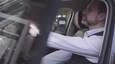 Kendine güvenen beyaz bir adamın sürücü koltuğunda oturup bakışlarını kaçırması. Başarılı bir iş adamı garanti tamiri sonrası aracı geri alıyor. Tamirhane, araba galerisi..