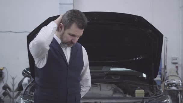 Portret zdenerwowanego białego biznesmena stojącego przed maską samochodu i myślącego jak mechanik samochodowy. Młoda pracownica dopingująca klienta zepsutym samochodem. Naprawa gwarancyjna, wypadek samochodowy. — Wideo stockowe