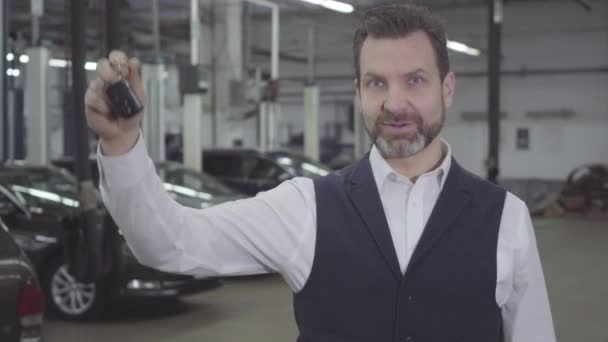 Porträtt av självsäker framgångsrik vit man som håller bilnycklarna i höger hand och tittar på kameran. Bilägare tar tillbaka fordonet efter reparation. Garantiservice, bilverksamhet. — Stockvideo