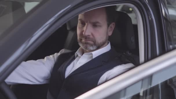 Cara de cerca del hombre caucásico adulto sentado en el asiento del conductor y revisando su coche después de la reparación. Exitoso hombre de negocios que recupera el vehículo después del servicio de garantía. taller de reparación, negocio de automóviles . — Vídeo de stock