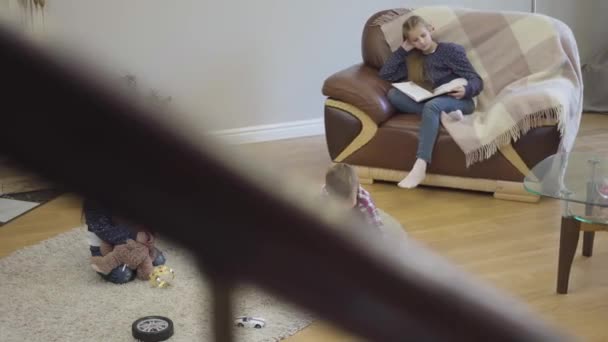 Shooting from stairs of playful Caucasian boy playing with toy car, his elder sister looking at siblings and smiling, and cute little girl looking at camera. Cheerful family resting on weekends. — Stock Video