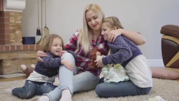 Portrait of happy Caucasian blond woman hugging and kissing daughters. Young mother taking care of her children indoors. Happiness, joy, leisure. Camera zooming in. — 비디오