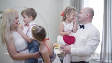 Büyük beyaz bir ailenin portresi evde duruyor, konuşuyor, kameraya bakıyor ve gülümsüyor. İçeride poz veren mutlu insanlar. Bir erkek ve bir kadın, çocukları büyük bir kız olarak ellerinde tutuyorlar..