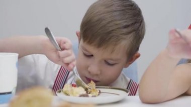 Lezzetli pasta yiyen küçük beyaz çocuğun yakın plan yüzü. Tatlı çocuk masada oturuyor ve tatlı yemeğin tadını çıkarıyor. Mutluluk, rahatlık, yaşam tarzı..