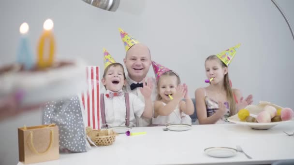 Kvinnliga vita händer med födelsedagstårta med figur fyrtio på bordet, vuxen man blåser ut ljus, barn kysser härlig far. Glad man firar med familjen hemma. — Stockvideo