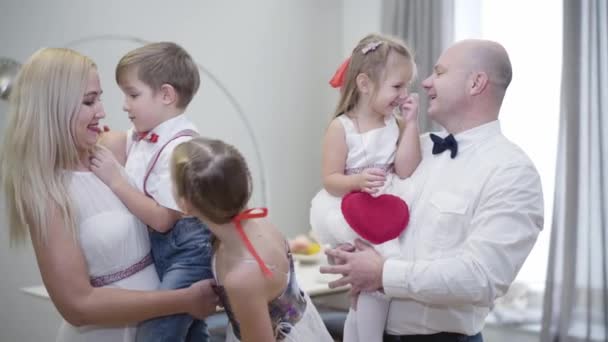 Portrait of big Caucasian family standing at home, talking, looking at camera and smiling. Happy people posing indoors. Man and woman holding children on hands as elder daughter standing between. — 비디오