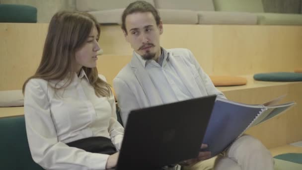 Primo piano di giovane caucasico uomo e donna seduti con computer portatile e documenti e parlare. Coworkers discutere di idee di business in ufficio creativo open space. Lavoro di squadra, imprenditori, startup . — Video Stock