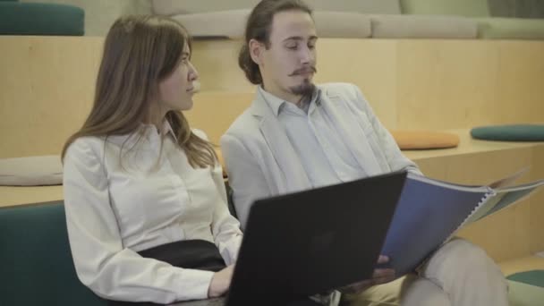 Zwei kaukasische Kollegen unterhalten sich und lächeln in einem modernen, komfortablen Großraumbüro. Positive Männer und Frauen, die Pause machen. Coworking, Unternehmer, Start-up, Kreativität. — Stockvideo