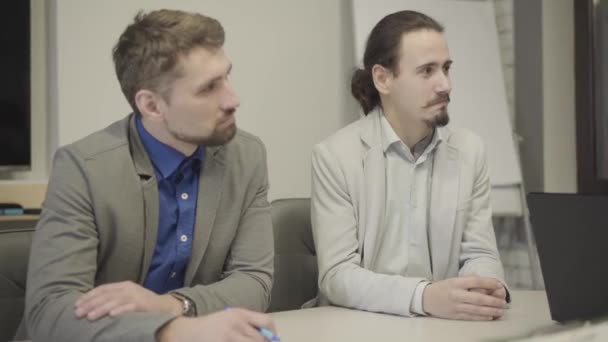 Camera approaching two male Caucasian office workers listening attentively as sitting at the table in the office. Portrait of adult coworkers at business meeting. Management, CEO, discussion. — 비디오