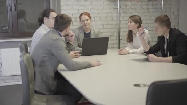 En grupp unga kaukasiska kollegor diskuterar projekt på öppna rymdkontor. Framgångsrika män och kvinnor som sitter runt bordet och delar idéer. Affärer, lagarbete, coworking. — Stockvideo
