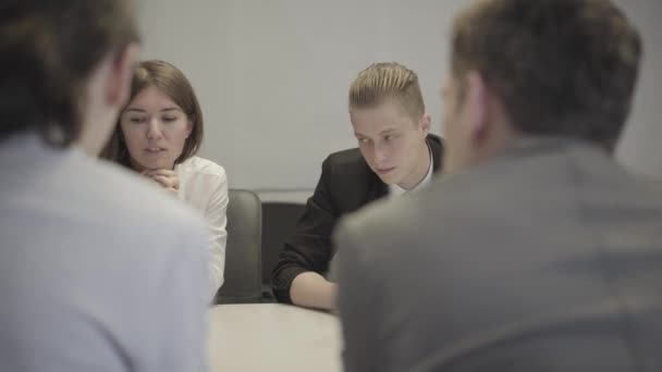 Portrait of young Caucasian woman and man sitting at business meeting and discussing project with colleagues. Female office worker sharing her ideas, guy listening carefully. Shooting over shoulder. — Stock Video