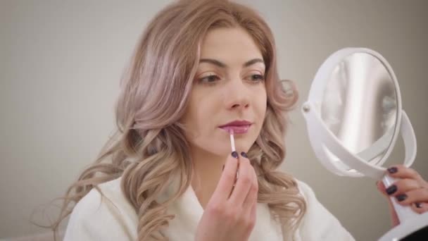 Close-up portret van charmante blanke meisje kijken naar kleine ronde spiegel en het aanbrengen van lippenstift. Zelfverzekerde jonge vrouw die zichzelf een kus stuurt in reflectie. Schoonheid, cosmetica, make-up. — Stockvideo