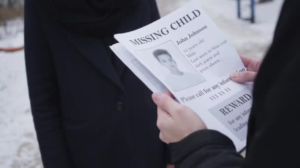 Um jovem caucasiano a dar anúncios de crianças desaparecidas a uma mulher irreconhecível na rua. O pai à procura do filho raptado. Perda, depressão, desespero . — Vídeo de Stock