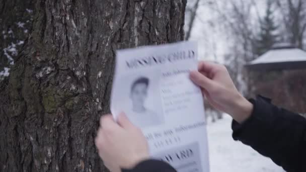 Bearded Caucasian man hanging missing boy ad on the tree. Young father searching for his lost son. Kidnapping, despair, social problems. — Stock Video