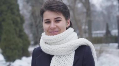 Kahverengi gözlü, kameraya bakıp gülümseyen güzel beyaz kadın portresi. Kışın açık havada duran beyaz eşarplı güzel bir kız. Yaşam tarzı, güzellik, mutluluk..