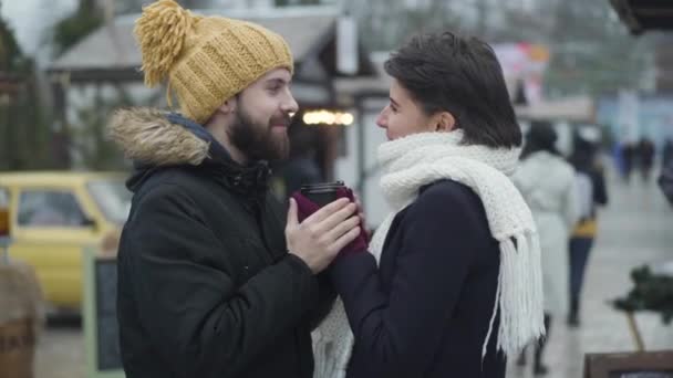 Boczny widok zakochanych mężczyzn i kobiet stojących na targach zimowych i patrzących na siebie. Brodatego chłopaka trzymającego dziewczyny za ręce i mówiącego. Jedność, miłość, styl życia. — Wideo stockowe