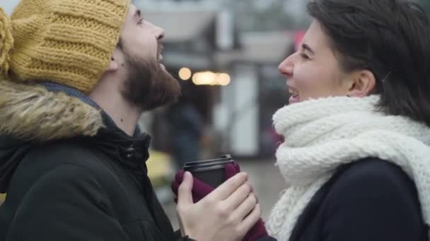 Close-up side view van het lachen Kaukasisch koppel met koffiebeker. Jongeman en vrouw die buiten staan te praten. Lifestyle, daten, vrije tijd. — Stockvideo