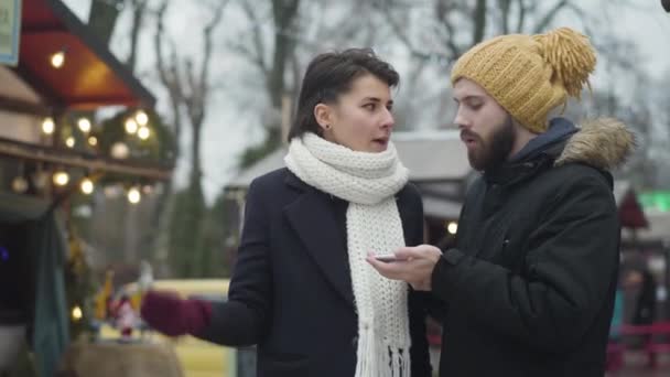 Irritated Caucasian woman talking with bearded husband or boyfriend on the street. Young couple disagree on the place to have dinner. Relationship problems, misunderstanding. — Stock Video