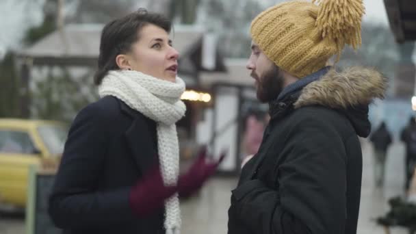 A fiatal kaukázusi család a szabadban vitatkozik. Gyönyörű barna nő és szakállas jóképű férfi beszél és gesztikulál érzelmileg áll a téli utcában. Tájékoztatási problémák. — Stock videók