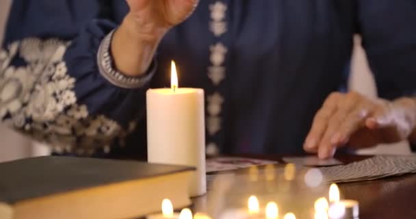 Close-up van de kaars staande op de tafel als wazig vrouwelijke blanke handen nemen van kaarten op de achtergrond. Onherkenbare vrouwelijke waarzegster leeskaarten. Bioscoop 4k Prores Hq. — Stockvideo