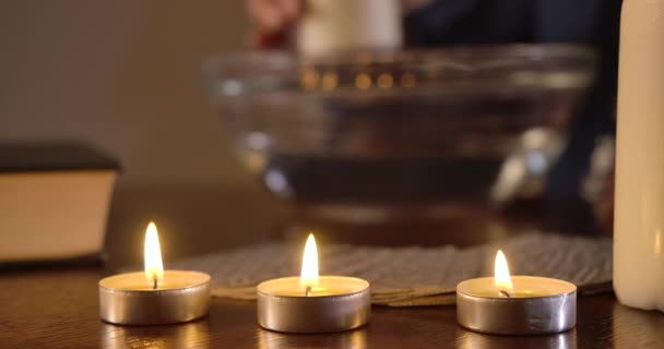 Primo piano di tre candele accese in piedi sul tavolo, carte distese dietro. Mano caucasica femminile che muove una grande candela attorno al piatto con acqua sullo sfondo. Magia, auguri. Cinema 4k ProRes HQ . — Video Stock