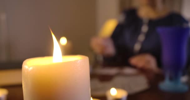 Detailní záběr zapálené svíčky stojící na stole jako rozmazaná běloška vybírající karty v pozadí. Kouzelnice čte osud na kartách. Cinema 4k Prores Hq. — Stock video