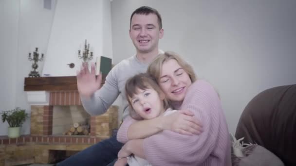 Young friendly Caucasian man, woman and little girl sitting on armchair and hugging. Smiling happy people posing indoors. Family, lifestyle, unity. — 비디오