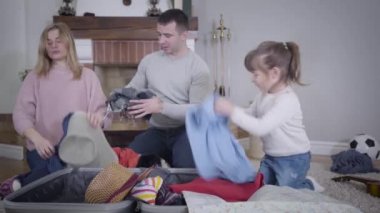 Oyunculuk taslayan beyaz bir kızın valizinden bir şeyler çıkarırken ebeveyn kıyafetlerini seyahat çantasına koyduğu portresi. Neşeli anne, yaramaz kızı şaka olsun diye azarlıyor. Aile, yaşam tarzı, turizm.