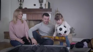 Ciddi küçük beyaz kız ukulele ve topu bavula koyup annemin seyahat çantasını kapatmasına yardım ediyor. Güzel kız, ailesiyle seyahat için bir şeyler hazırlıyor. Yaşam tarzı, çocukluk, turizm.