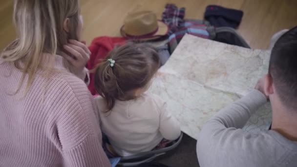 Genç beyaz bir ailenin haritaya bakışıyla. Dost canlısı baba, anne ve kız yolculuk için rota çiziyor. Turizm. Yaşam tarzı, mutluluk. — Stok video