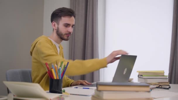 Portré fiatal barna kaukázusi fiú nyitó laptop, integetett és mosolygott. Magabiztos férfi diák videochatel. Modern technológiák, online kommunikáció. — Stock videók