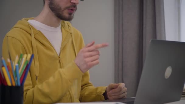 Jeune homme caucasien méconnaissable assis à la table devant un ordinateur portable et parlant. Étudiant barbu ayant chat vidéo en ligne. Concept d'éducation, technologies modernes . — Video