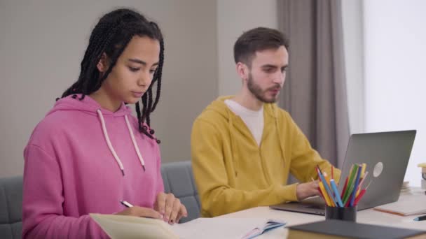 Side view of blurred Caucasian boy using laptop and asking for advice from beautiful African American girl. Groupmates studying together. Education, learning, intelligence. — Stock Video
