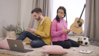 Cute African American girl looking back at boyfriends smartphone and pushing his shoulder. Upset girlfriend arguing with Caucasian boy indoors. Trust, online communication, lifestyle.