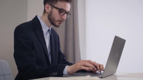 Retrato de vista lateral de belo homem de negócios caucasiano em óculos digitando no laptop. Jovem homem inteligente em terno elegante trabalhando online. Estilo de vida, trabalho, inteligência . — Vídeo de Stock