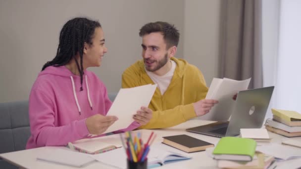 Retrato de estudantes multiétnicos alegres vomitando papéis e rindo. Menina afro-americana feliz e menino caucasiano se divertindo enquanto estudava. Felicidade, educação, estilo de vida. Movimento lento . — Vídeo de Stock