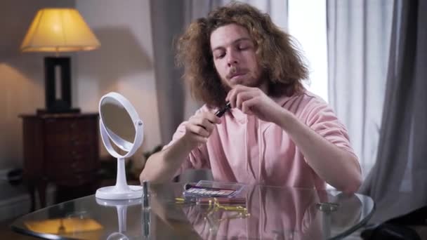 Midden schot van de jonge blanke man die mascara opent en naar de borstel kijkt. Man intersex persoon kiezen make-up cosmetica binnen. Zelfbeeld, genderidentiteit. — Stockvideo