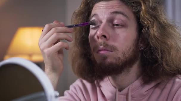 Spodní pohled na bělošskou intersexuální osobu, která používá oční stíny. Vousatý muž s dlouhými vlasy a make-upem. Transgender, ženskost, životní styl. — Stock video