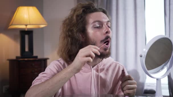 Kobiecy biały mężczyzna nakładający różową szminkę na twarz z makijażem. Problem percepcji osób interseksualnych, tożsamości płciowej. — Wideo stockowe