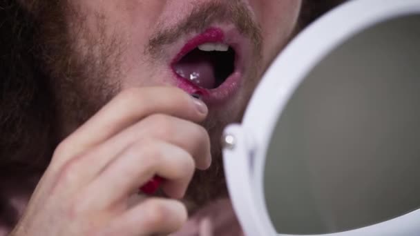 Extreme close-up of male hand applying red lipstick on one side of lower lip. Intersex person expressing both sides of self perception. Binary gender, minority problems, self identification. — Stock Video